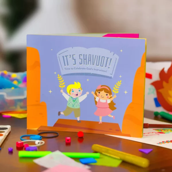 The Shavuot children's book standing up on a table surrounded by colorful craft supplies.