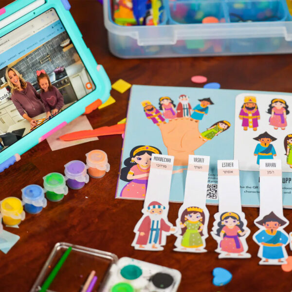 A table filled with craft supplies and an iPad with video instructions to the Purim book craft.